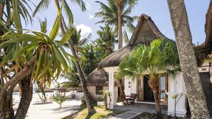 A beachfront property with a thatched-roof house, palm trees, and a sandy beach. - Constance Sakoa Boutik (Trou aux Biches)