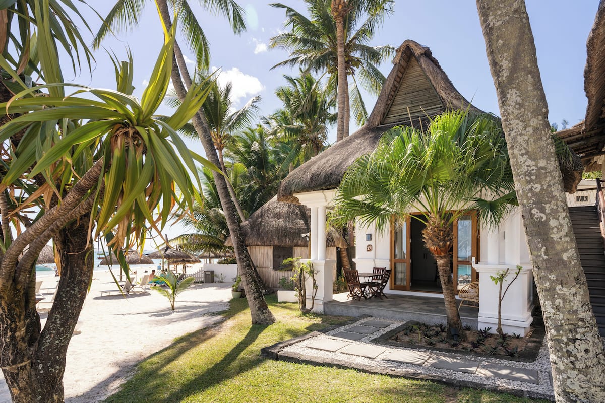 A beachfront property with a thatched-roof house, palm trees, and a sandy beach.