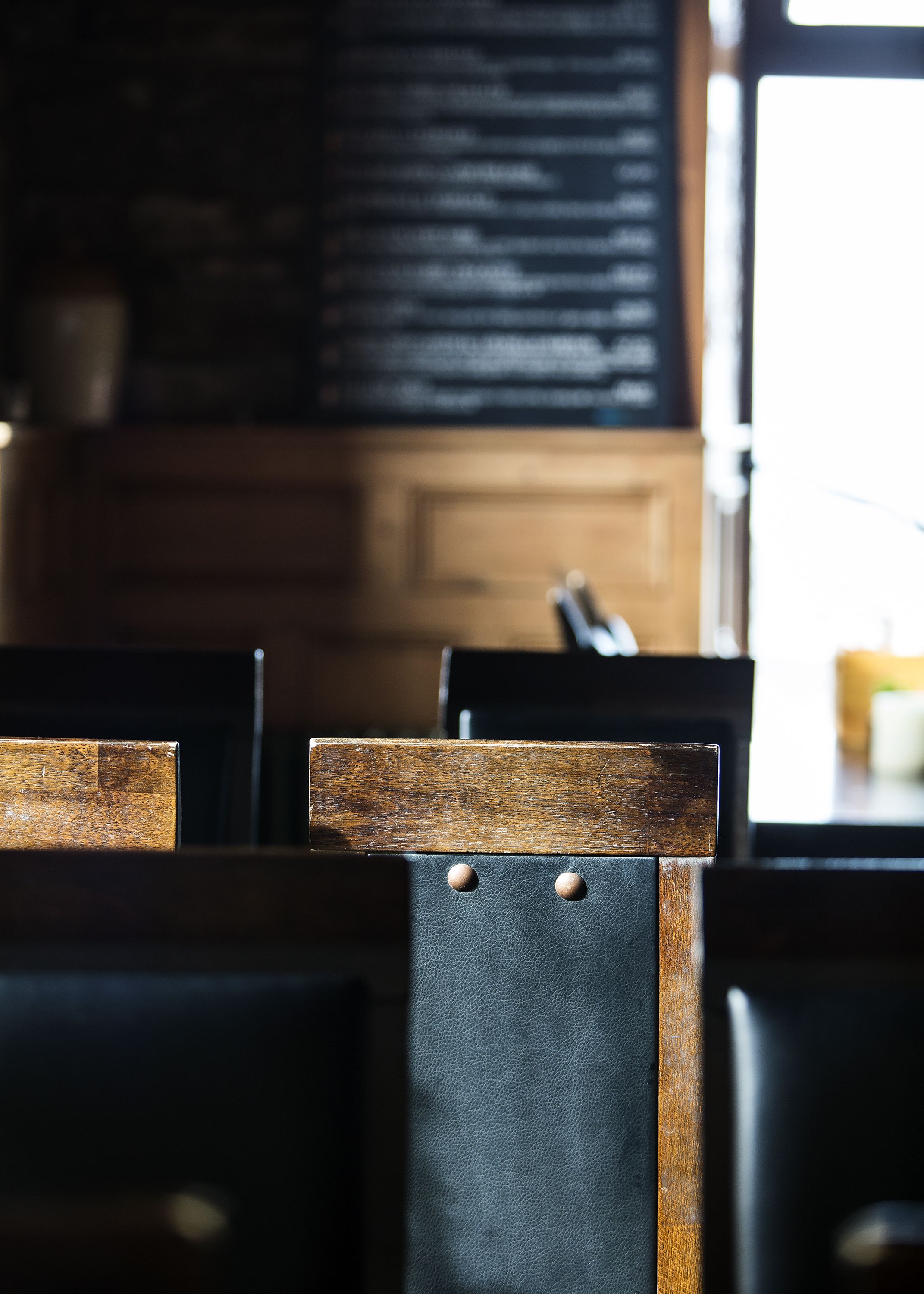 A close-up of a wooden chair with a leather backrest and metal rivets.