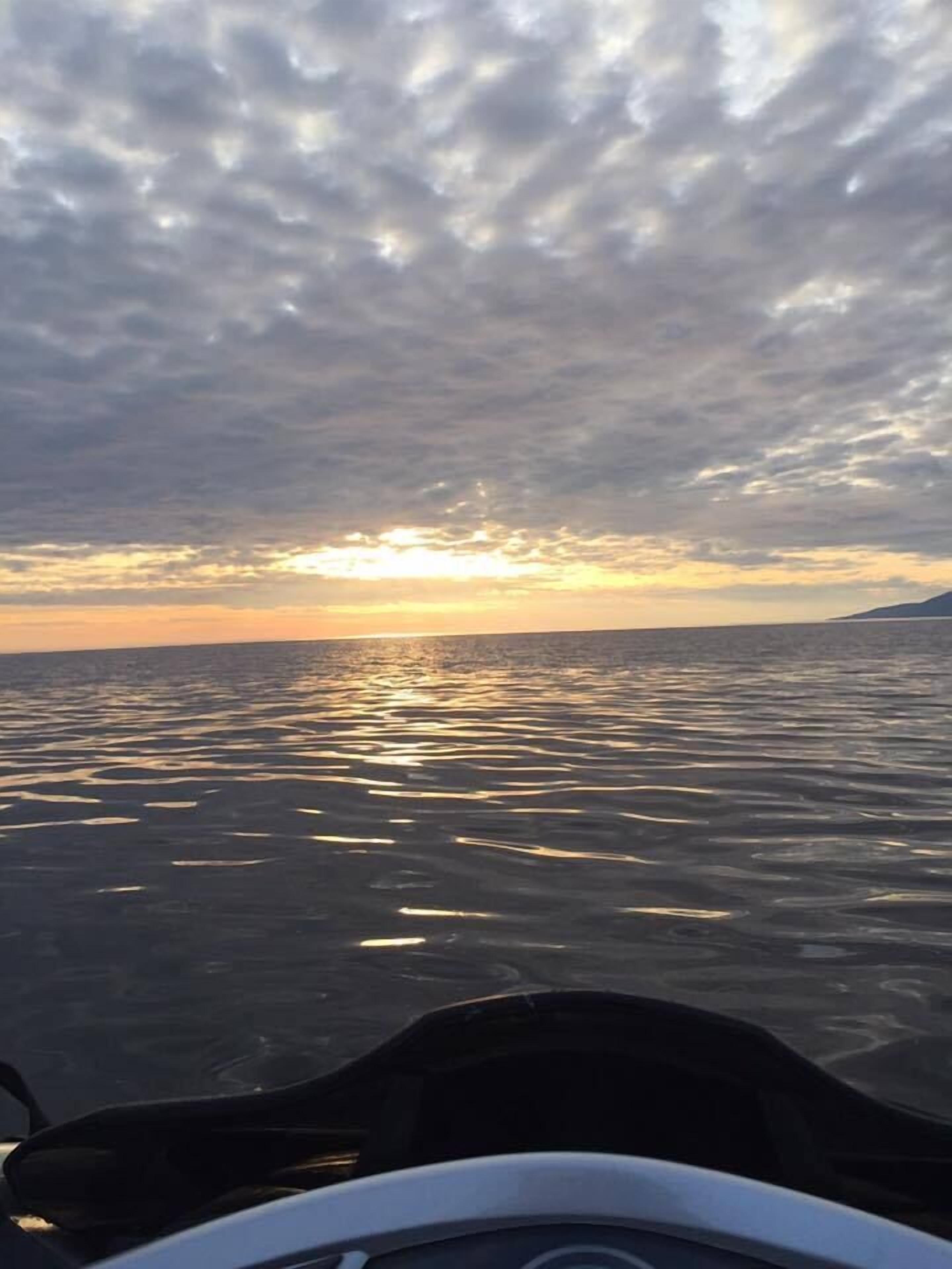 A view of the ocean with a cloudy sky and the sun setting or rising.