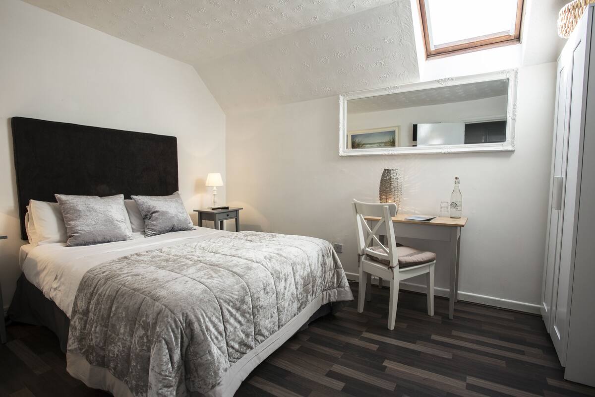 Un dormitorio con cama, escritorio, silla, lámpara y espejo.