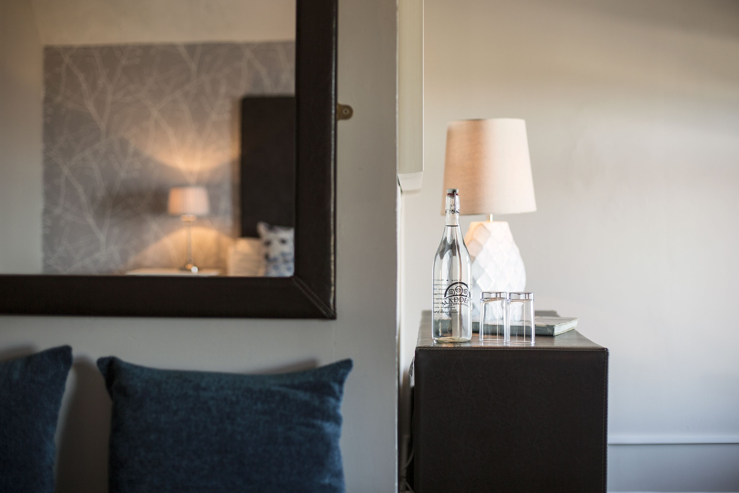 A hotel room with a dark wooden nightstand, a lamp, and a bottle of water.