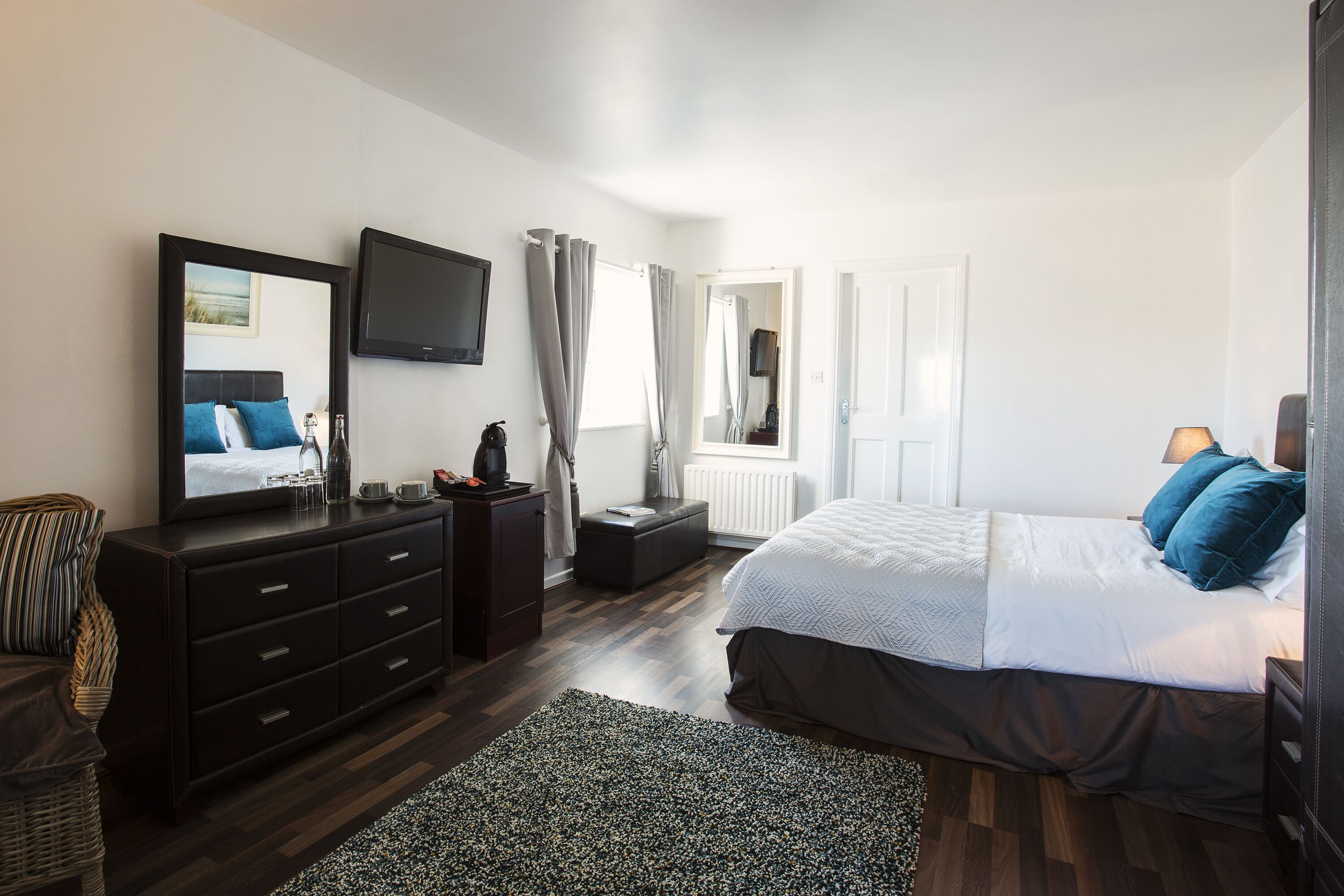 A bedroom with a bed, a dresser, a television, and a window with curtains.