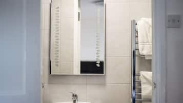 Casa de banho com lavatório branco, espelho e porta-toalhas.