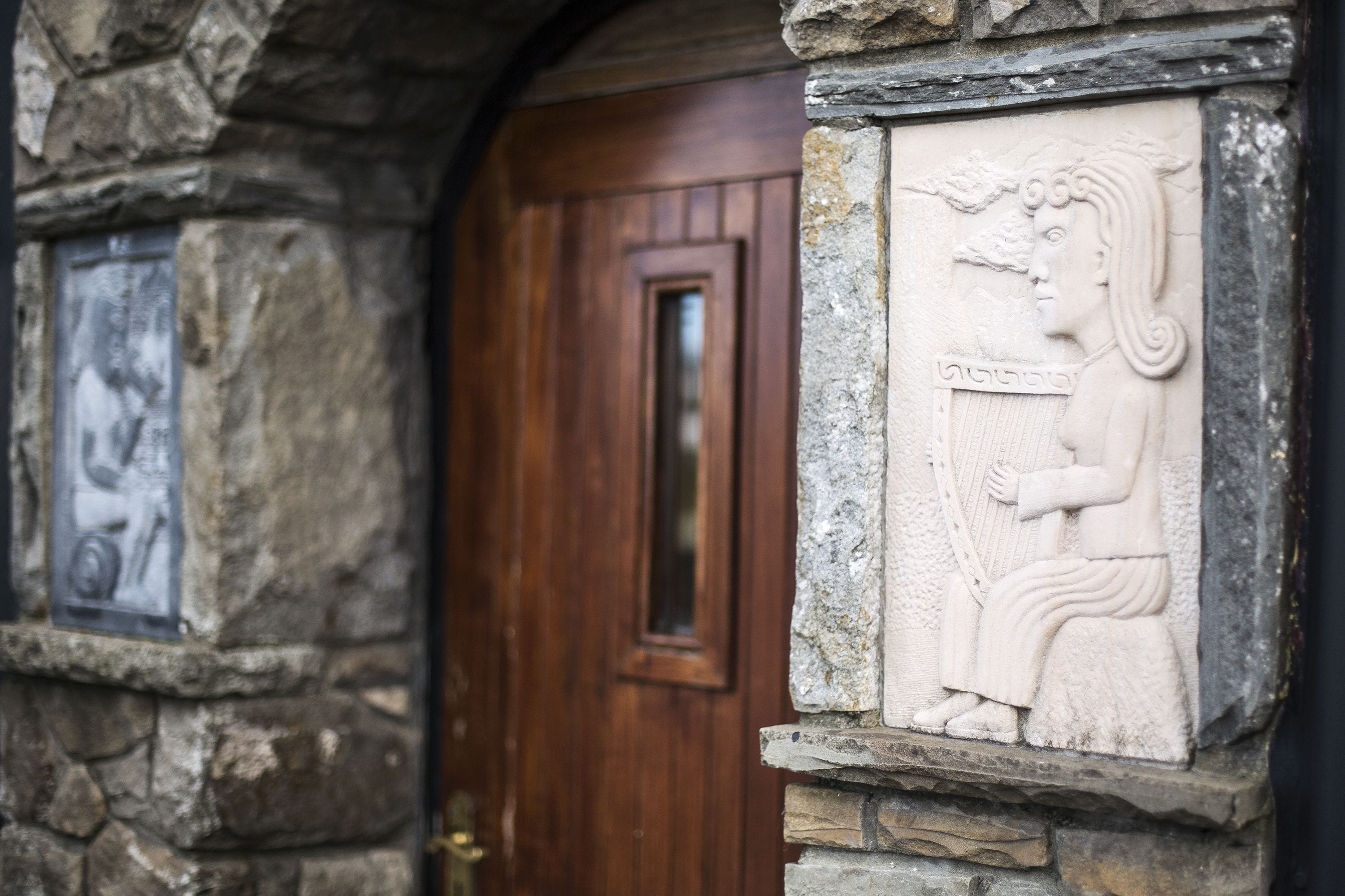 A stone doorway with a carved relief of a figure holding a staff, a wooden door, and a stone plaque with a picture.