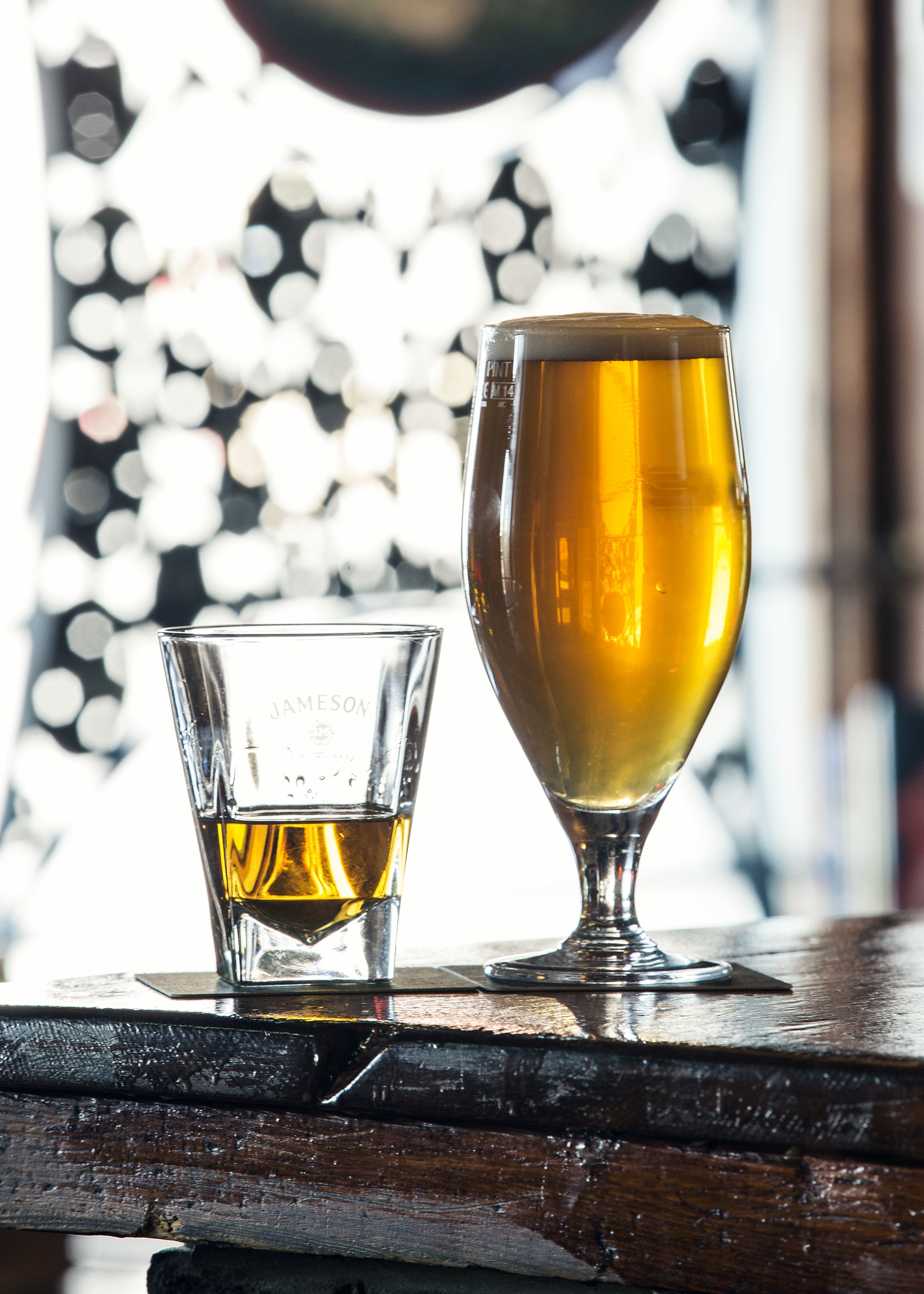 Deux verres contenant un liquide ambré sont posés sur une surface en bois, avec un arrière-plan flou présentant des motifs circulaires.