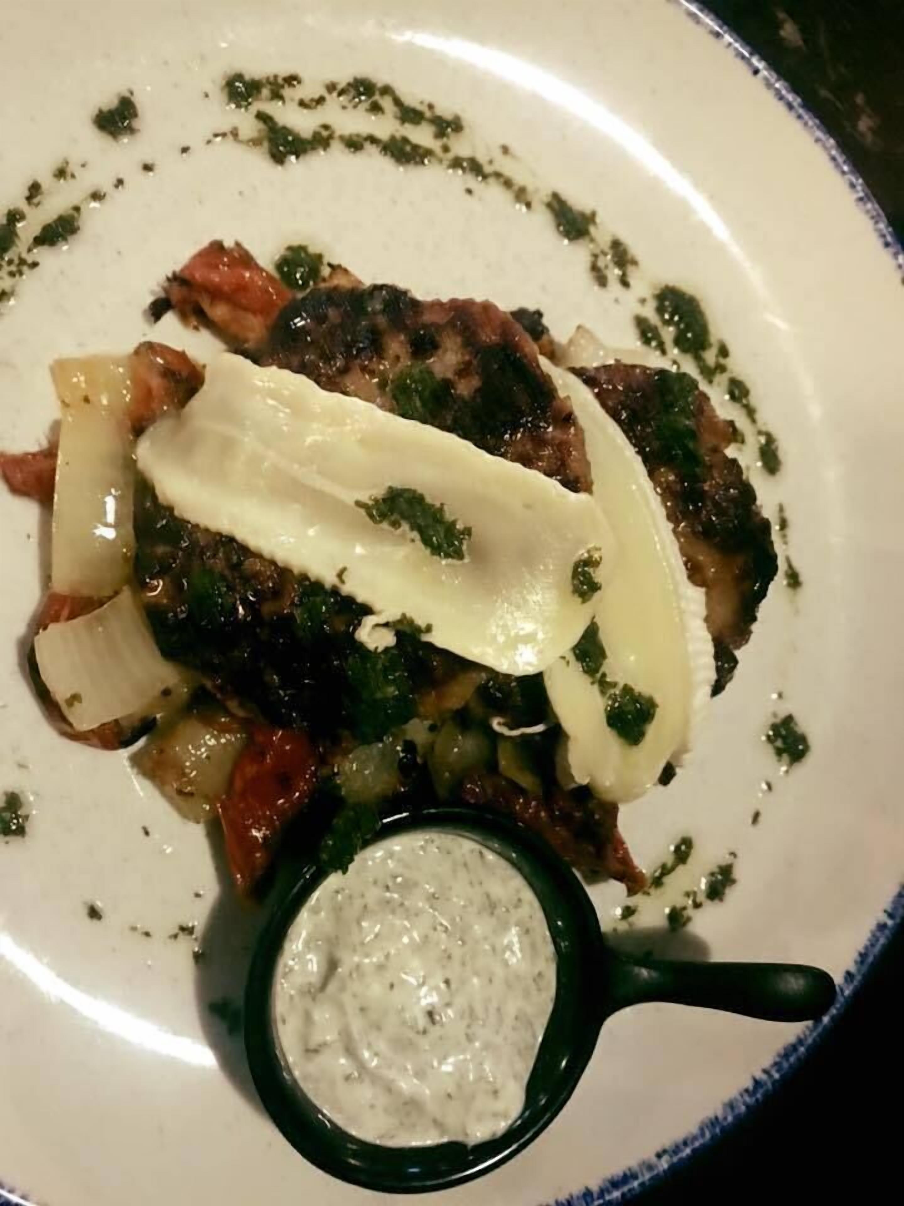 A plate with grilled chicken, vegetables, and a small bowl of sauce.