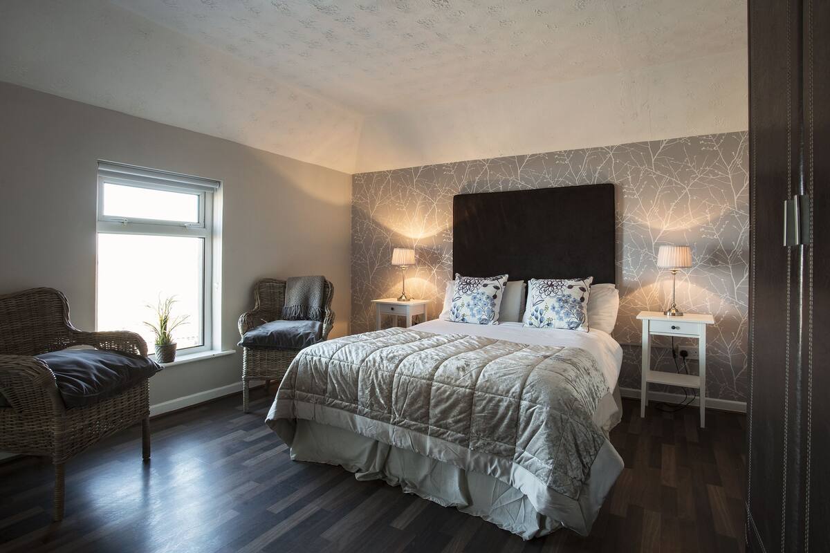 Un dormitorio con una cama grande, dos mesitas de noche, una silla y una ventana.