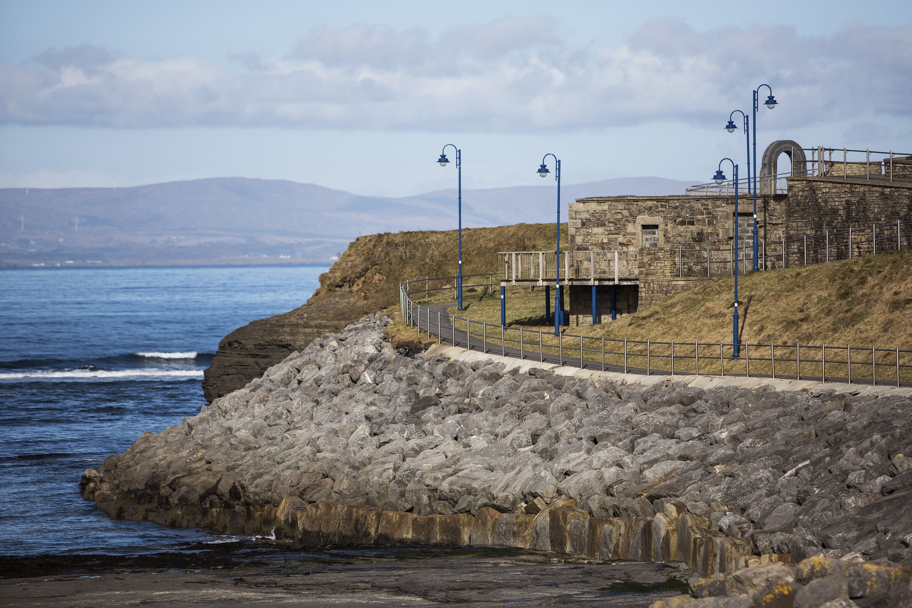 A coastal stone structure with a pathway and railing, overlooking the sea.