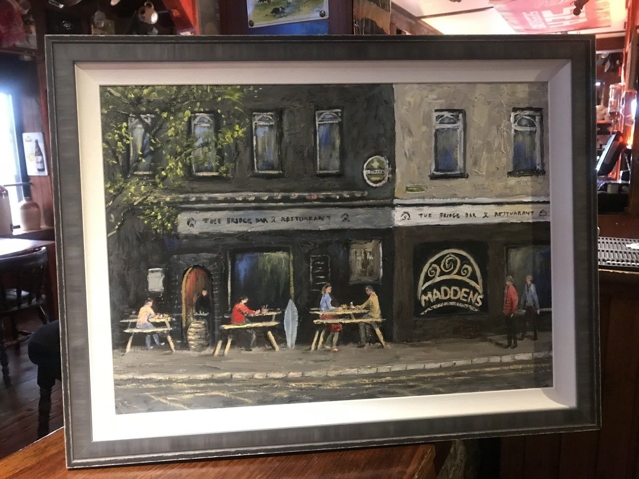 A framed painting of a street scene with tables and people.