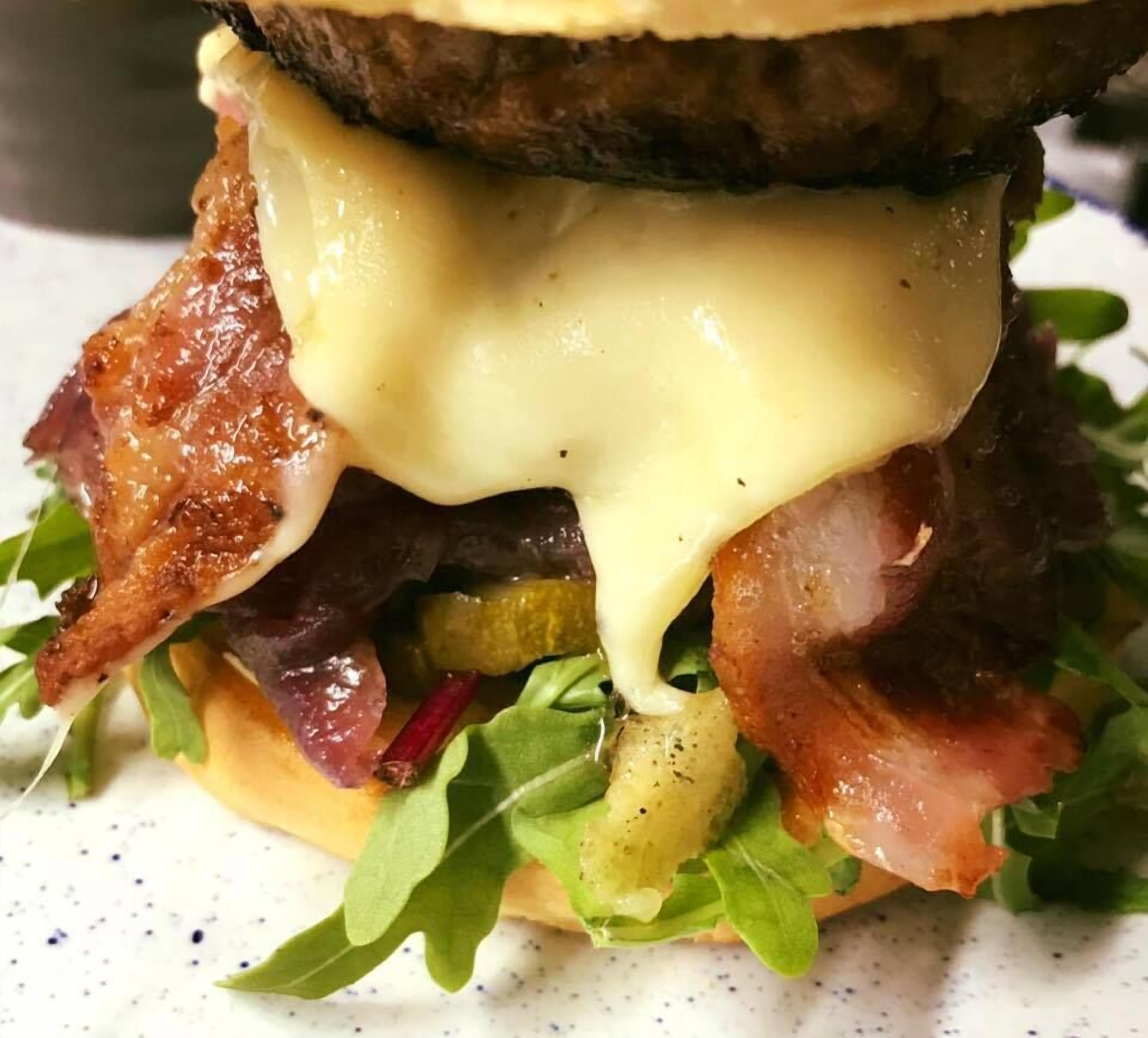 A sandwich with bacon, cheese, and greens.