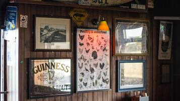 Un bar rústico con paredes de madera, un letrero con forma de tabla de surf, cuadros enmarcados y un letrero de Guinness.
