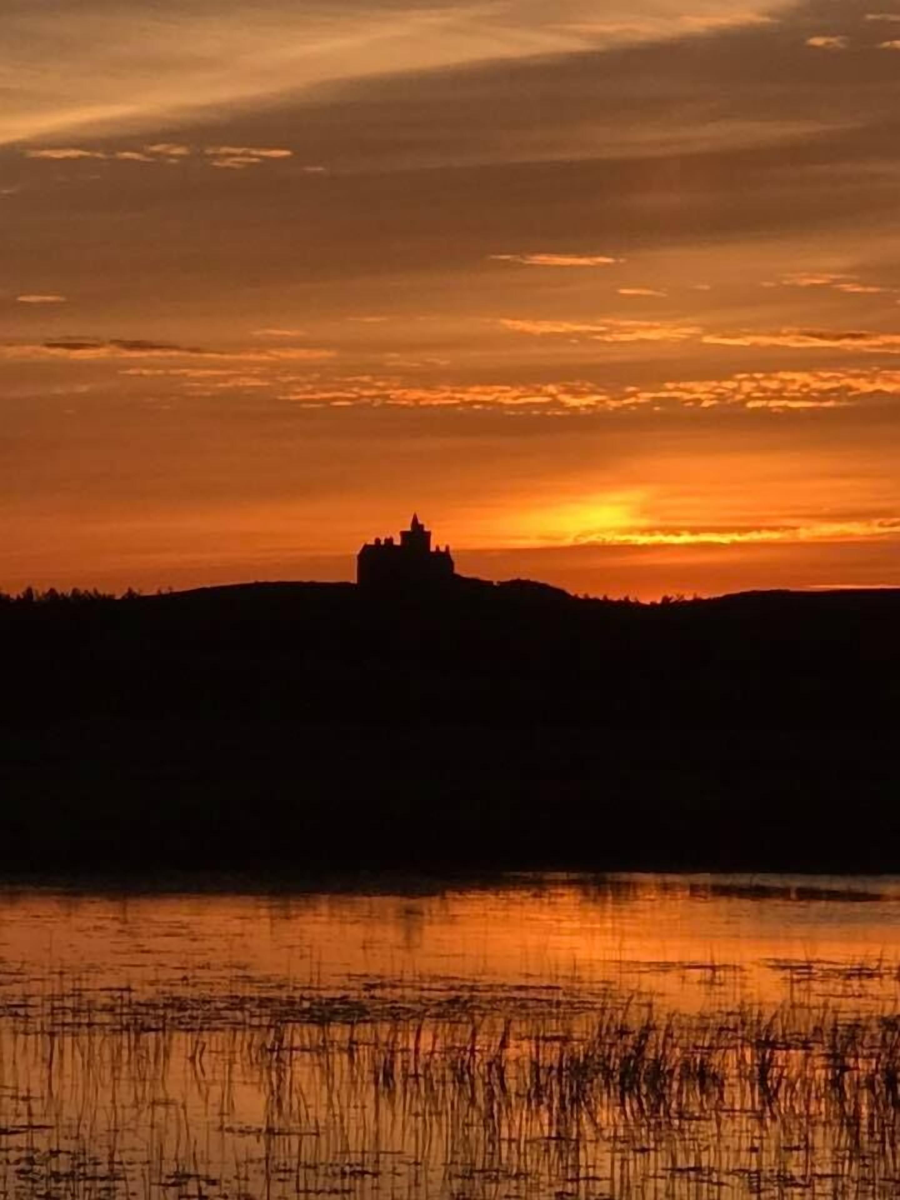 Silueta de un castillo contra un cielo al atardecer, con una masa de agua al frente.