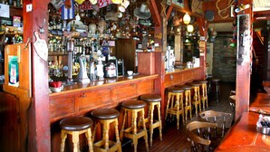 Een bar met houten krukken, een toog en verschillende flessen en decoraties.