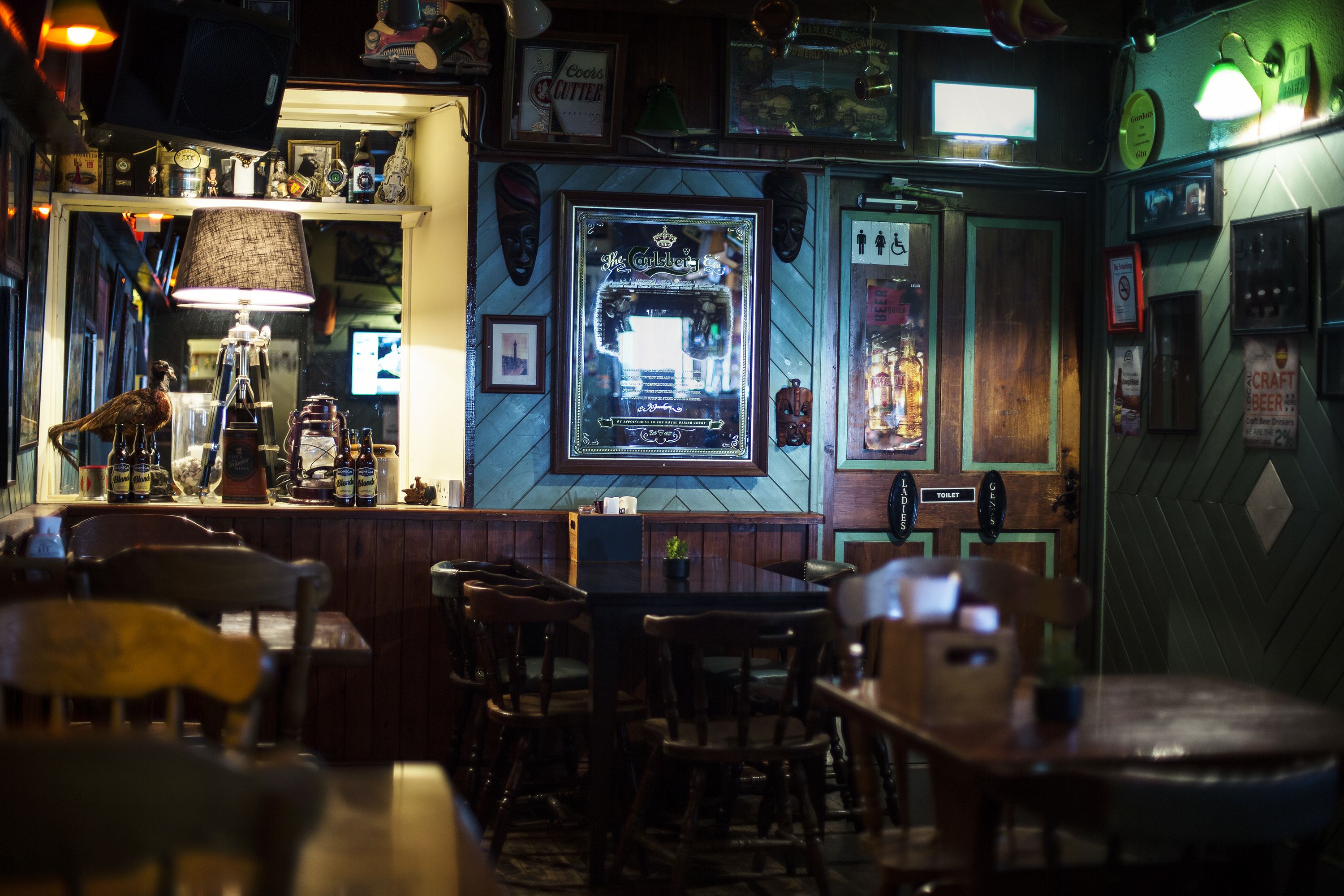Zona de bar con mobiliario de madera, barra y varias decoraciones, incluyendo cuadros enmarcados y un letrero de neón.