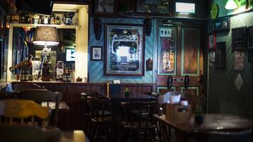 Zona de bar con mobiliario de madera, barra y varias decoraciones, incluyendo cuadros enmarcados y un letrero de neón.