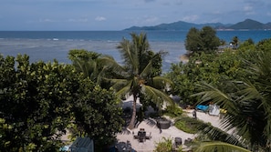 A beachside view with a dining area, palm trees, and a view of the sea and mountains.