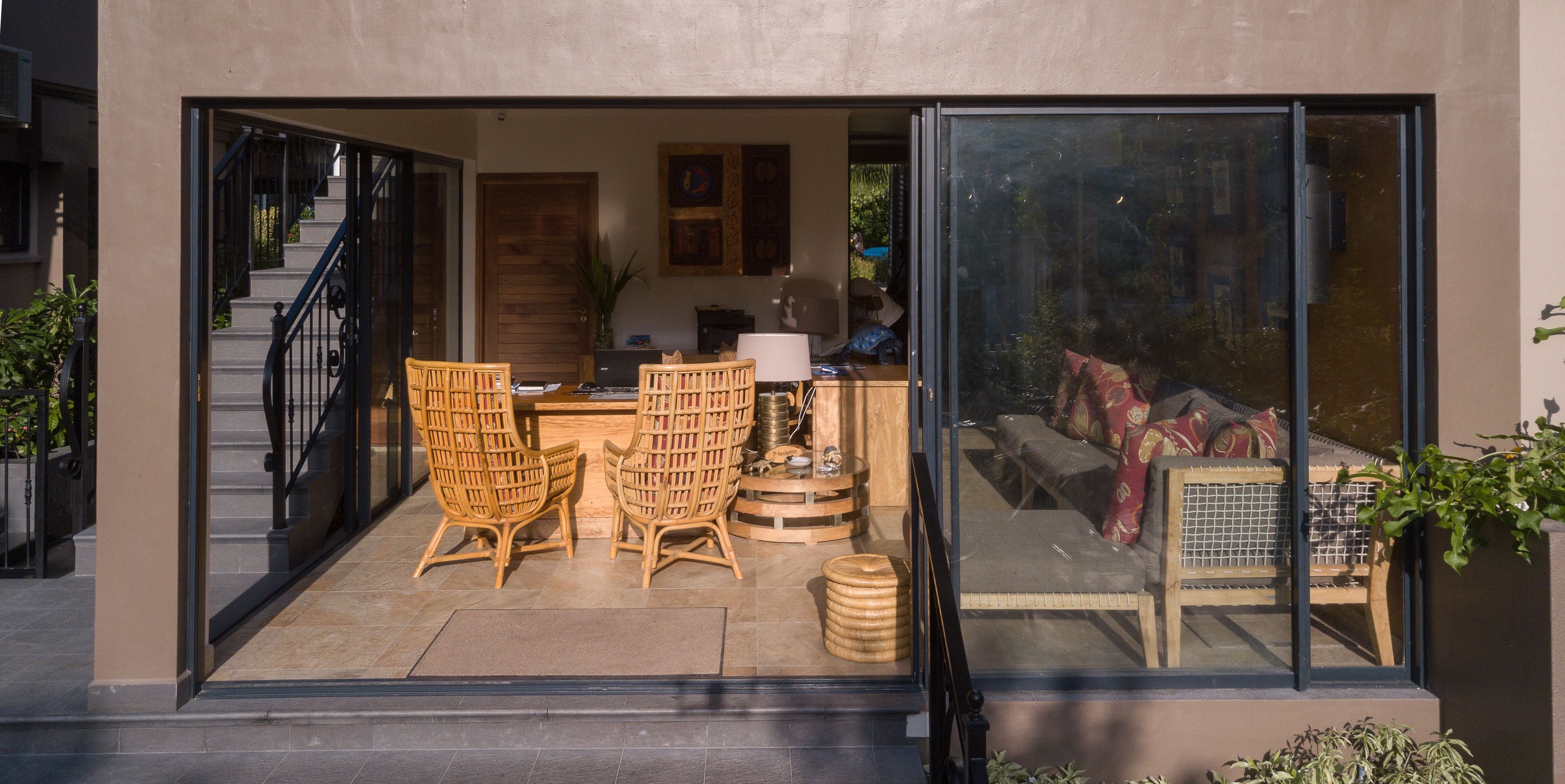 Un interior moderno con una puerta de vidrio que da a una sala de estar con muebles de mimbre, un sofá y una mesa de centro.