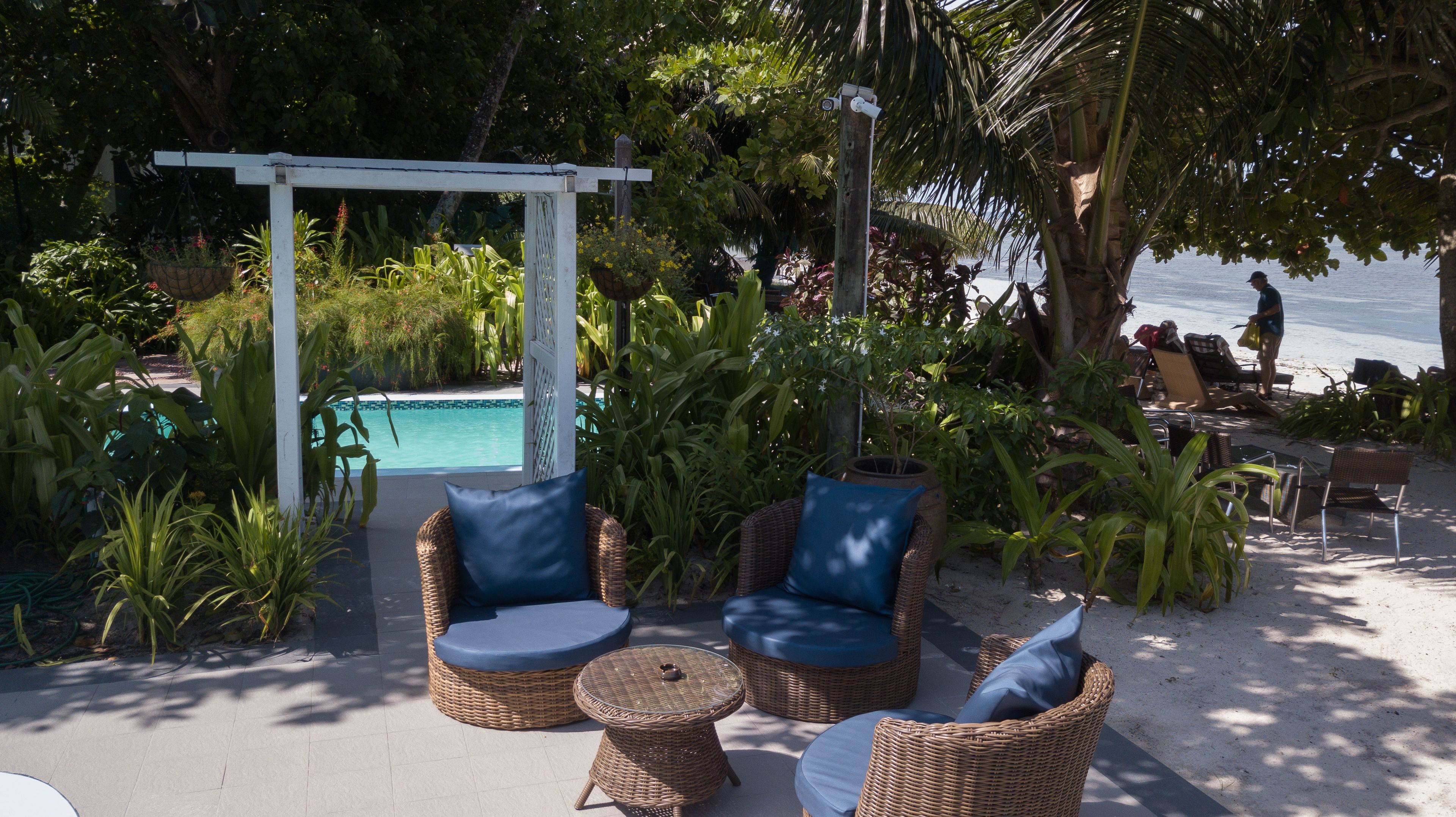 Un área junto a la piscina con mobiliario de mimbre y una pérgola.