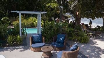 Un área junto a la piscina con mobiliario de mimbre y una pérgola.
