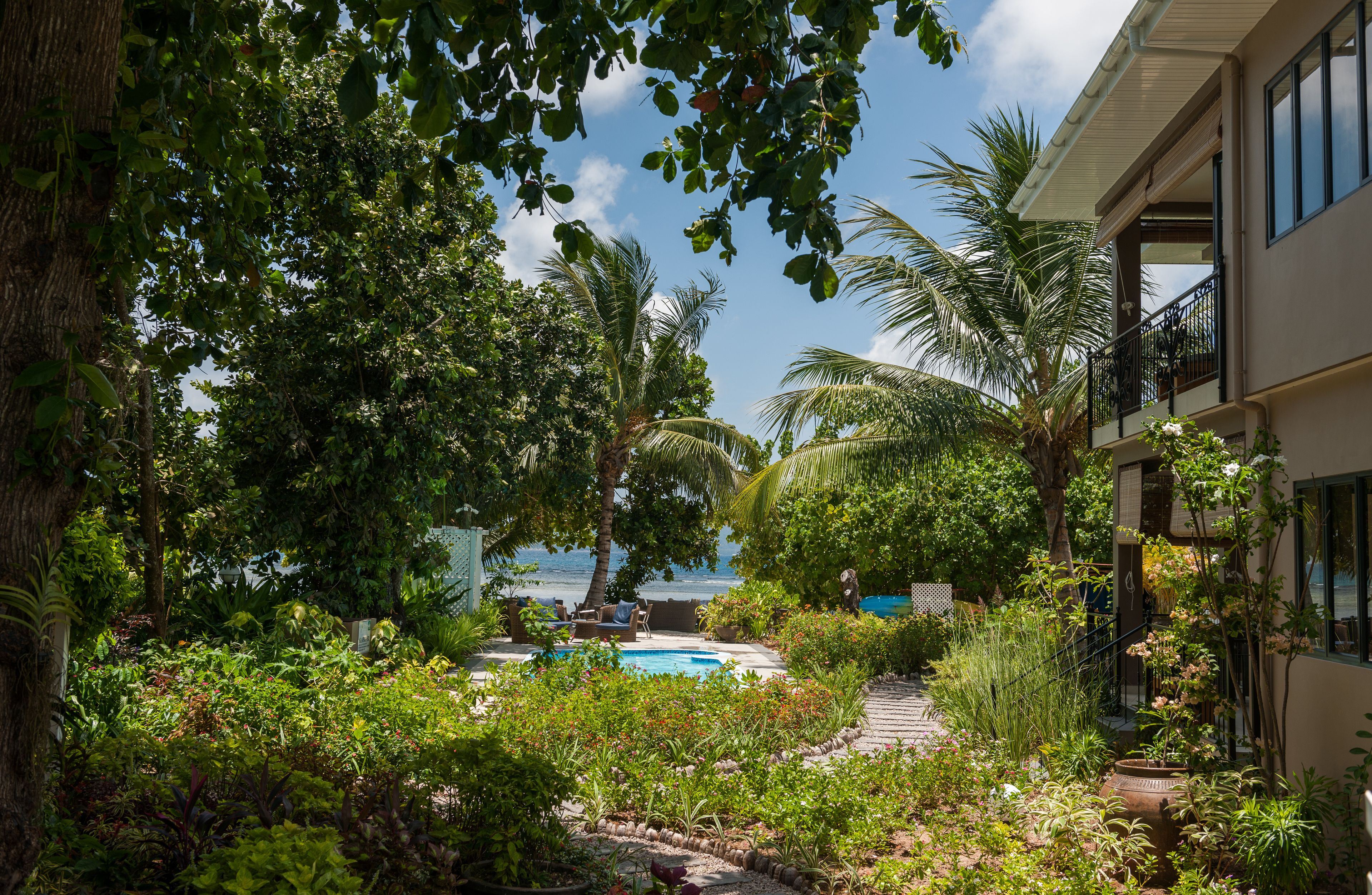 A pool area with a view of the ocean, surrounded by lush greenery and palm trees.