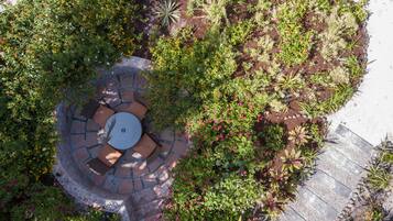 Luchtbeeld van een tuin met een rond terras van steen en een zithoek, omgeven door diverse planten en bloemen.