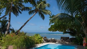 Une piscine avec vue sur l’océan, entourée de palmiers et de chaises longues.