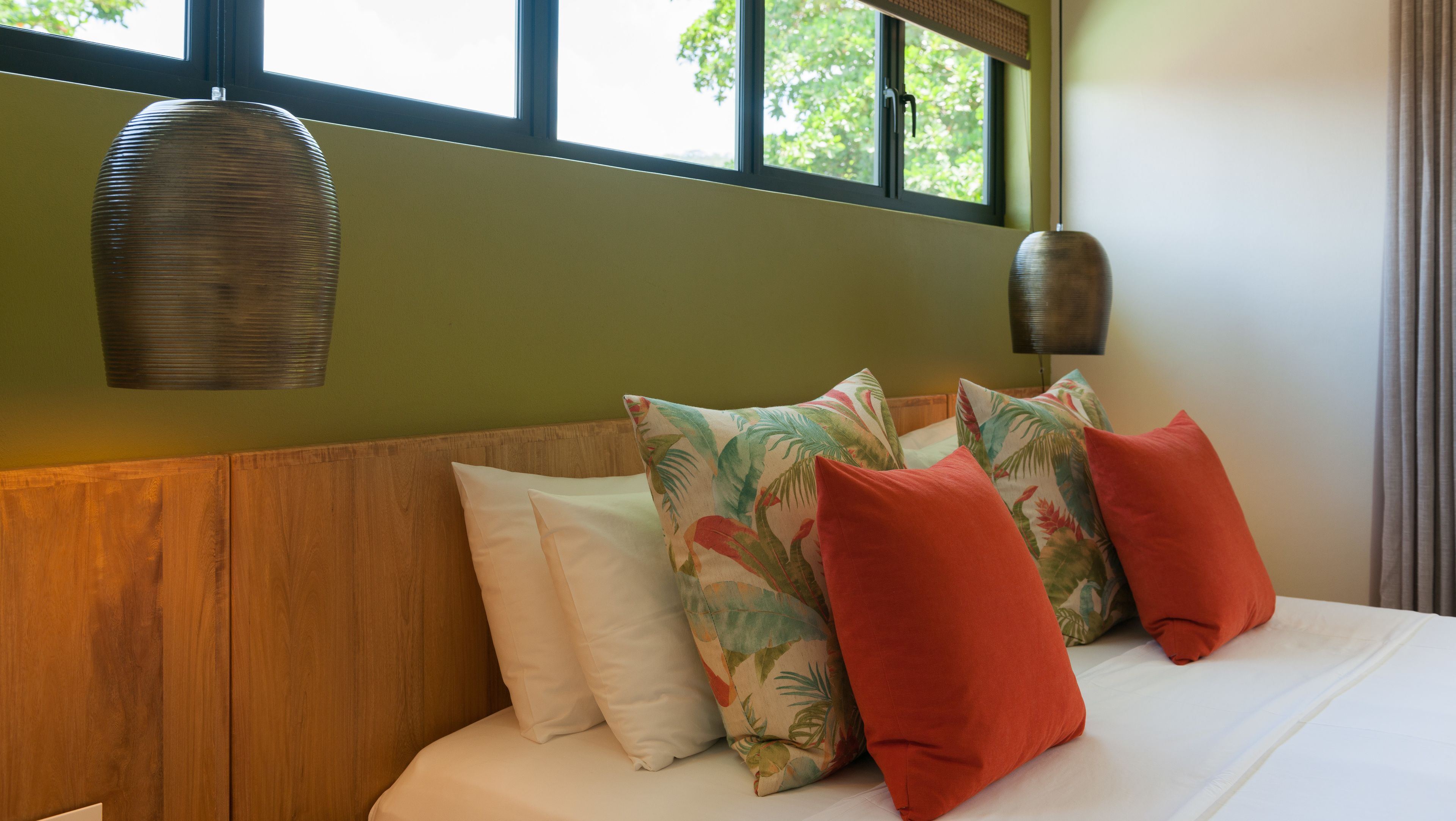 A bedroom with a wooden headboard, a bed with white bedding, and tropical-themed pillows.
