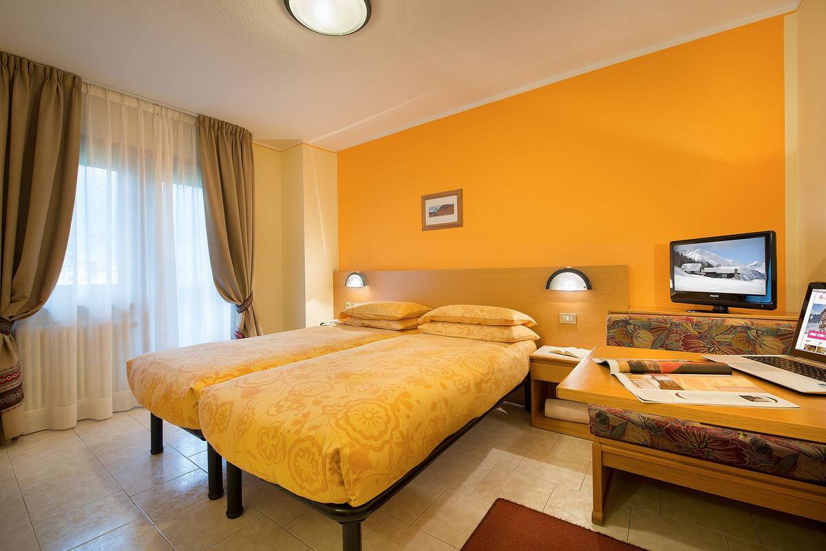 A hotel room with two beds, a desk, a computer, and a television.