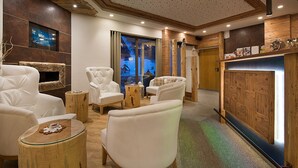 A modern lounge area with leather sofas, a fireplace, and a large window with a view of a snowy landscape. - Garnì Oasi (Livigno)