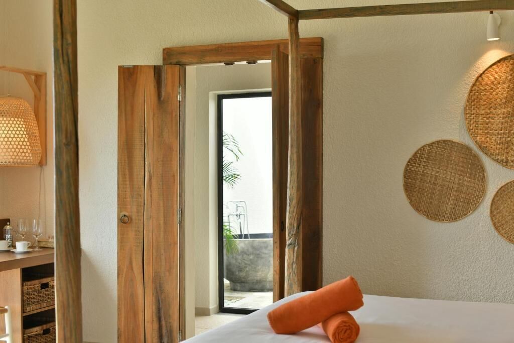 Hotelkamer met een houten deur die leidt naar een buitenruimte, een bed met een oranje handdoek en een wand met wanddecoratie.