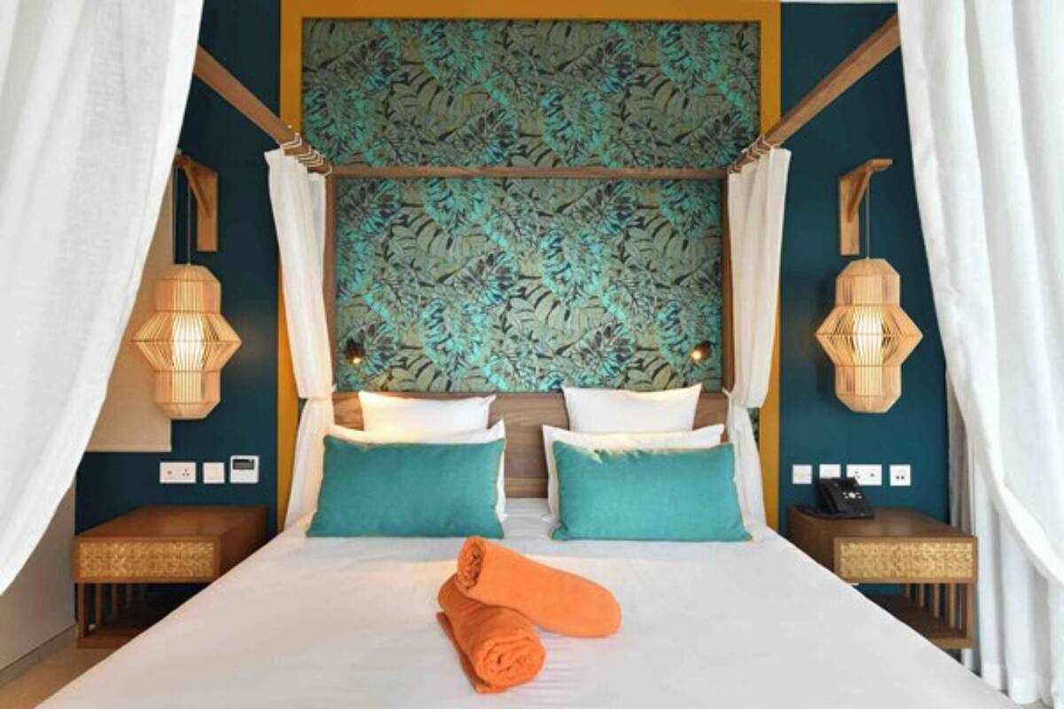Une chambre d’hôtel avec un grand lit, deux tables de chevet, une tête de lit ornée d’un motif végétal et deux lampes fixées au mur.