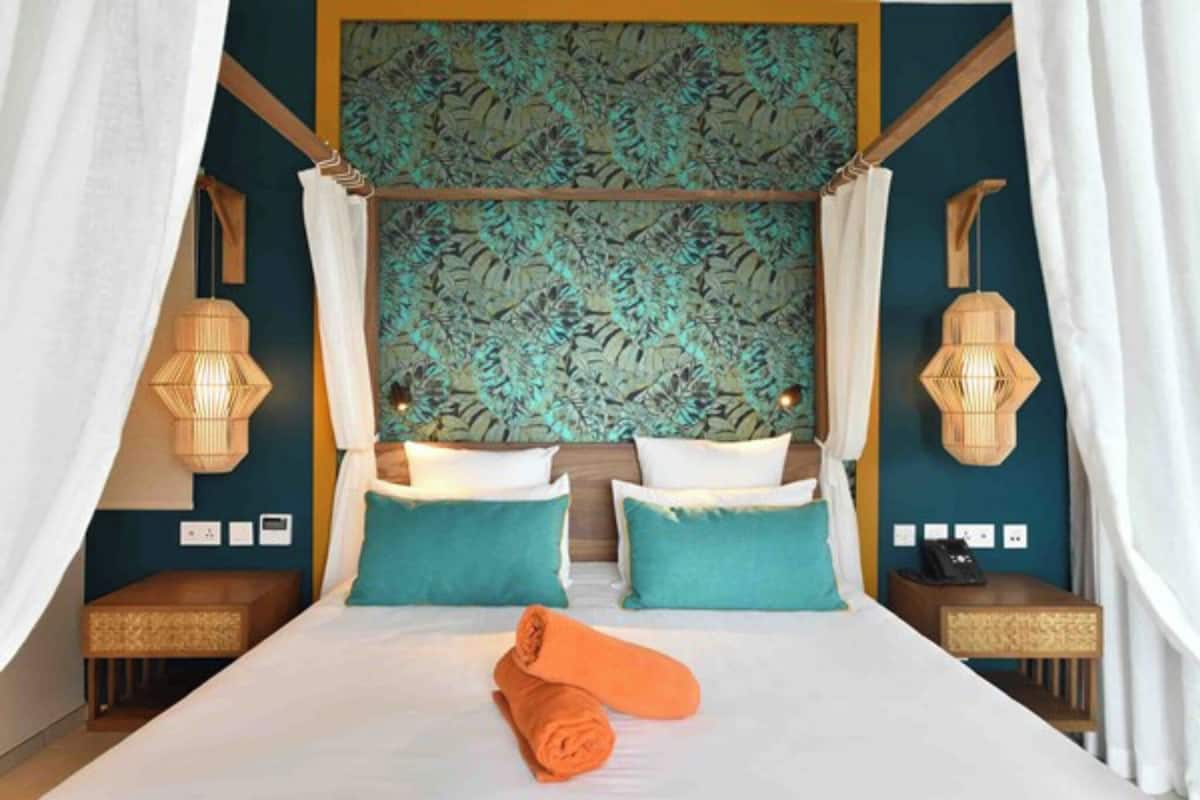 Ein Hotelzimmer mit einem großen Bett, zwei Nachttischen, einem Blattmuster an der Kopfteil und zwei Wandleuchten.