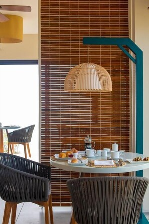 A dining area with a round table set for four, featuring a woven pendant light and a wooden slatted wall in the background. - Constance Tekoma. Rodrigues (Rodrigues Island)