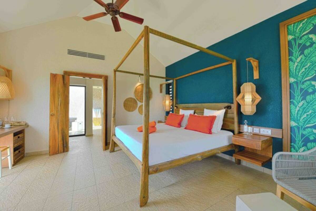 Un lit à baldaquin avec un cadre en bois, un ventilateur de plafond et une vue sur l’intérieur de la pièce.