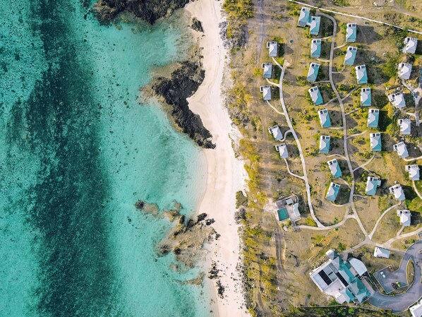 An aerial view of a coastal resort with multiple bungalow-style buildings, a sandy beach, and clear turquoise waters. - Constance Tekoma. Rodrigues (Rodrigues Island)