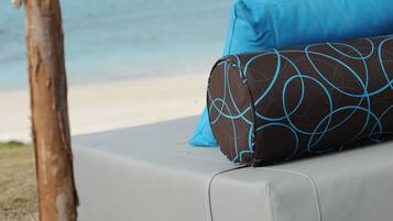 A beachside lounge with a view of the ocean, a white canopy, and a blue pillow.