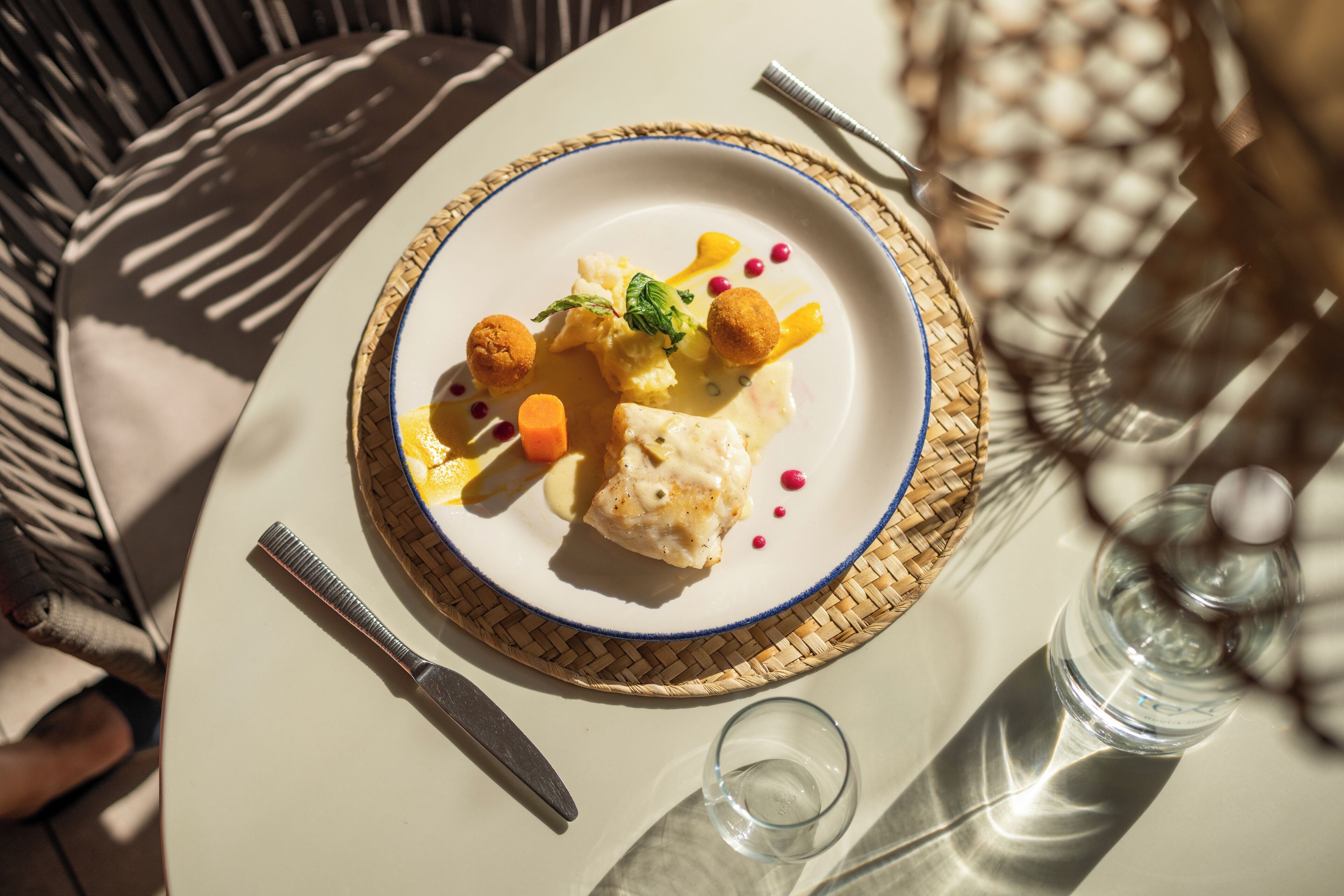 A dining table with a plate of food, a knife, a glass, and a fork.