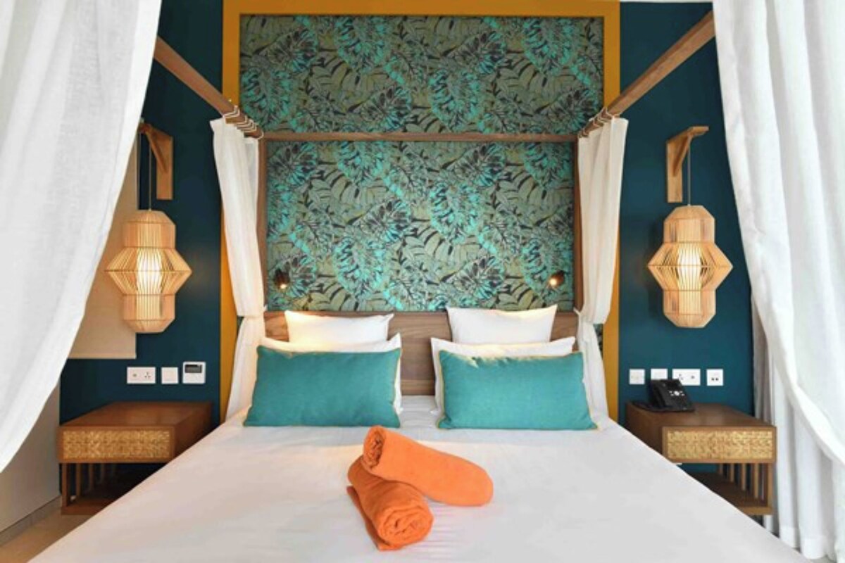 Habitación de hotel con una cama grande, dos mesitas de noche, un cabecero con motivos vegetales y dos lámparas de pared.