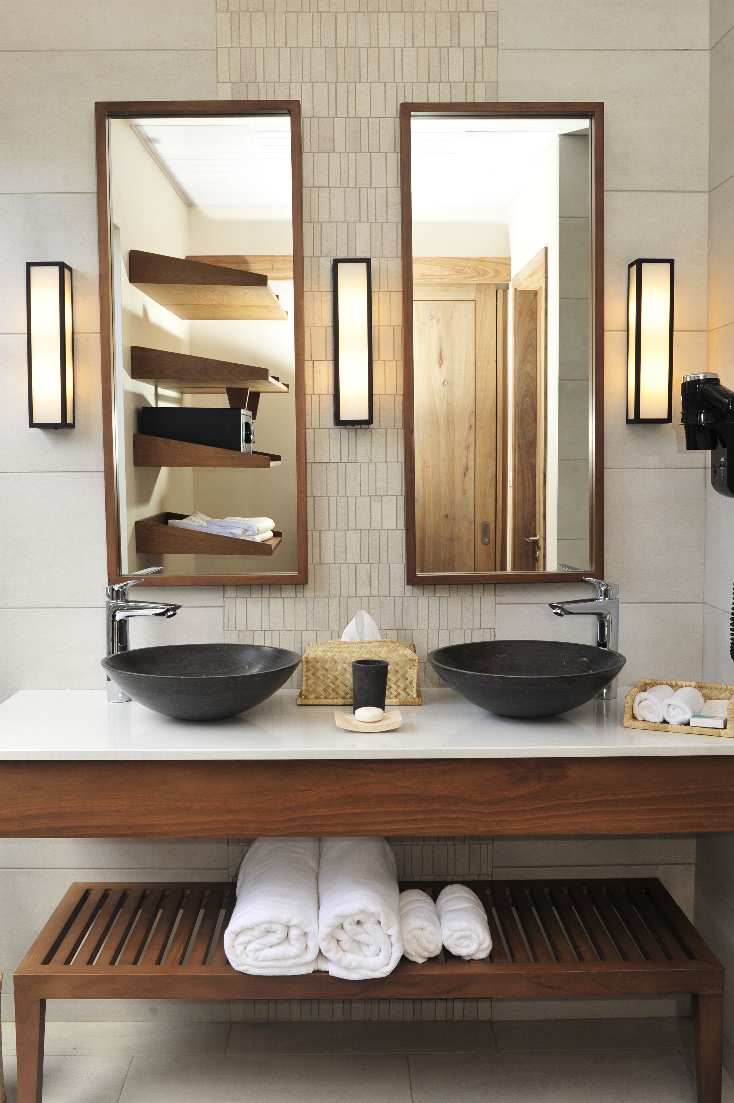 A bathroom with two large mirrors, a wooden vanity, and a towel rack.