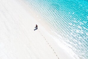 A beach with clear turquoise water and a person walking along the shore. - Constance Tekoma. Rodrigues (Rodrigues Island)