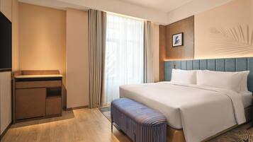 Habitación de hotel con cama, una banca, escritorio y un amplio ventanal con cortinas.