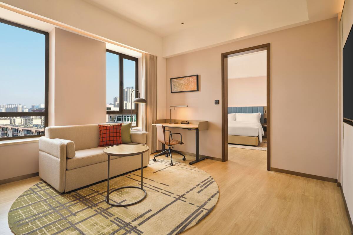 Una habitación de hotel moderna con sofá, una mesita redonda, escritorio y cama.
