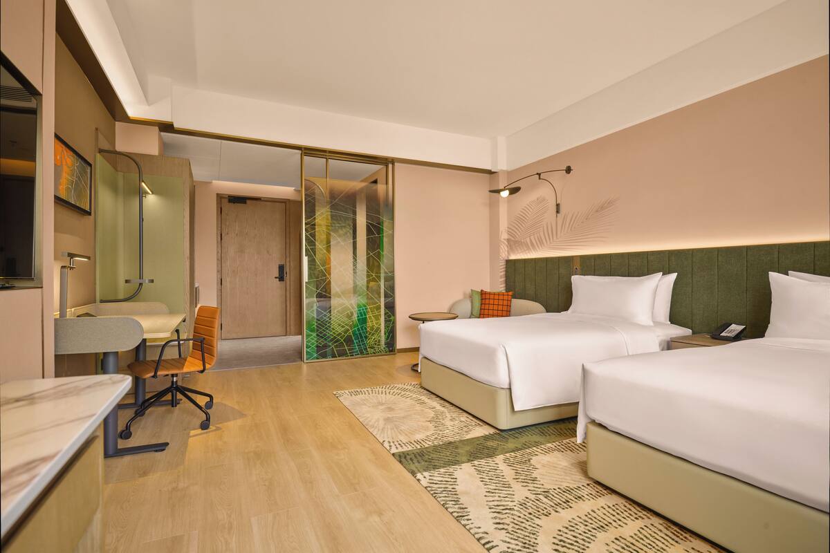 Una habitación de hotel moderna con un escritorio, dos camas, una silla y un espejo grande.