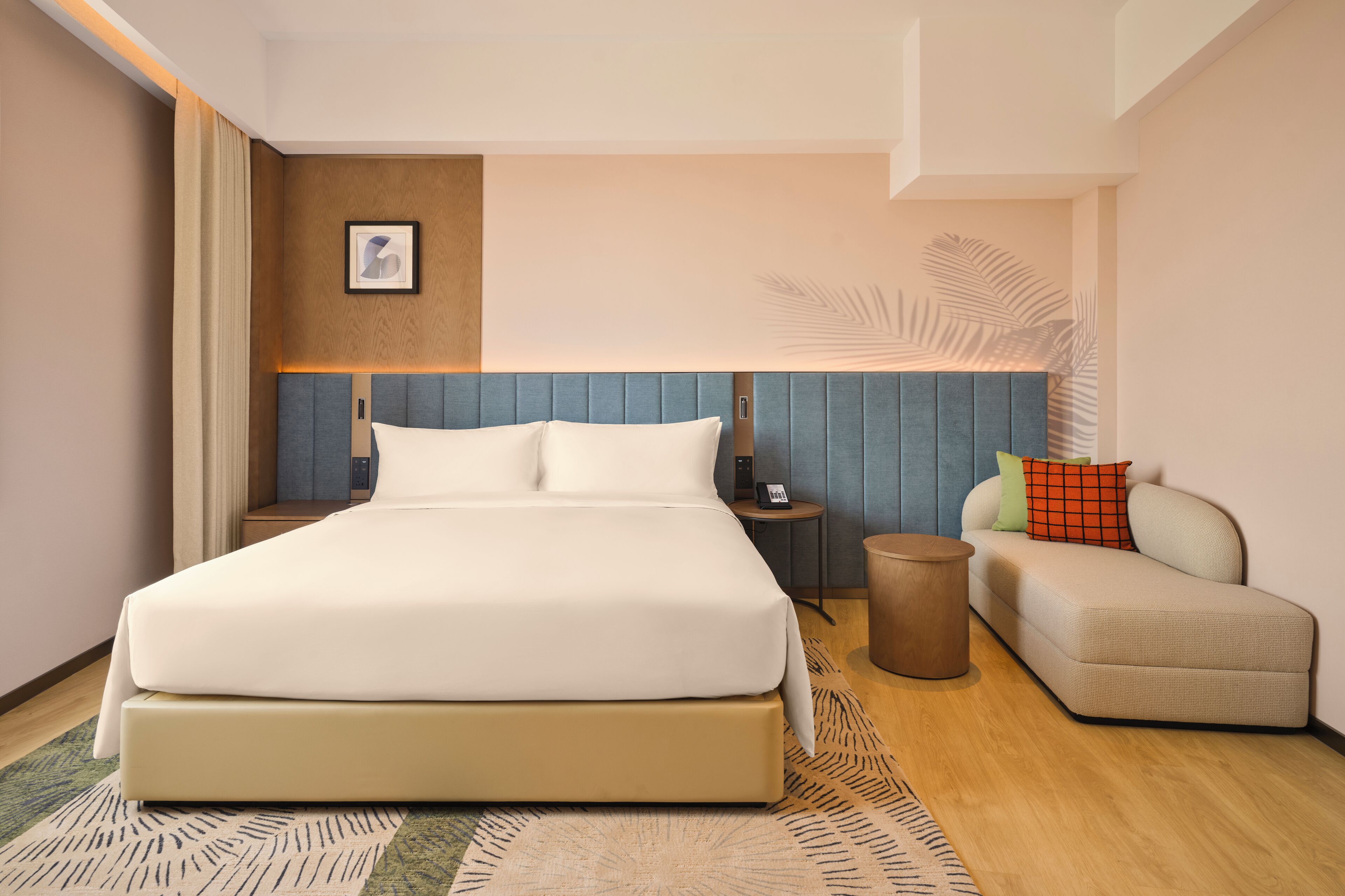 A modern hotel room with a large bed, a sofa, a small side table, and a decorative wall panel.