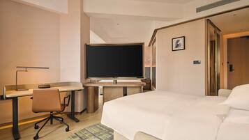 A hotel room with a bed, a desk with a chair, a flat-screen TV, and a door.