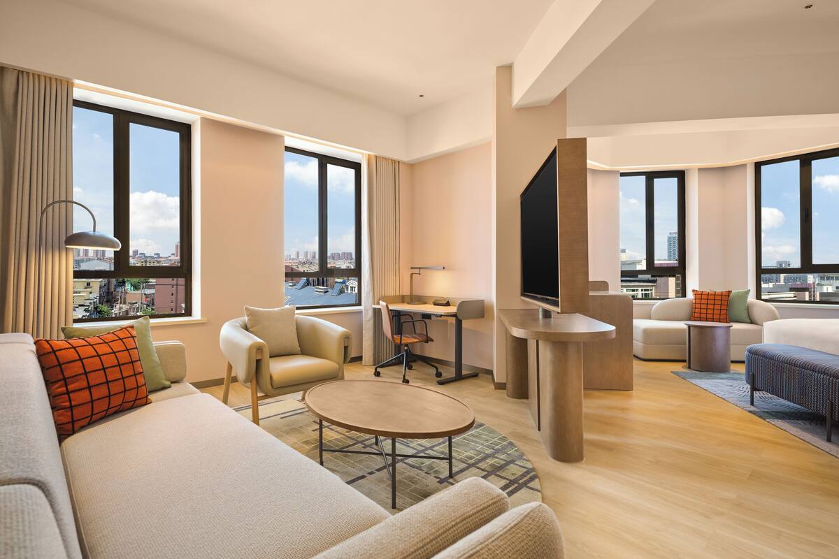 Una habitación de hotel moderna con un ventanal grande, un sofá, una mesa de comedor y un televisor.