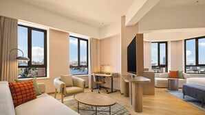 Una habitación de hotel moderna con un ventanal grande, un sofá, una mesa de comedor y un televisor.