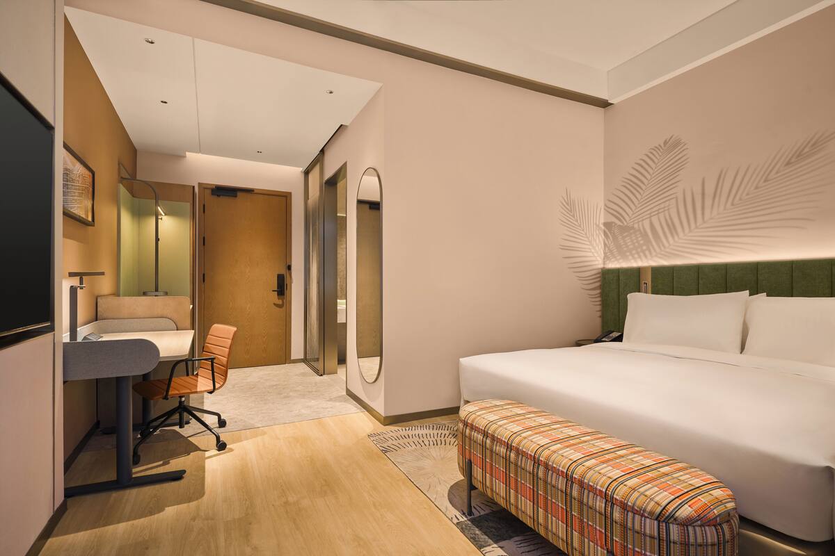 Habitación de hotel con cama, escritorio, silla, banco, espejo y pared con diseño de hojas.