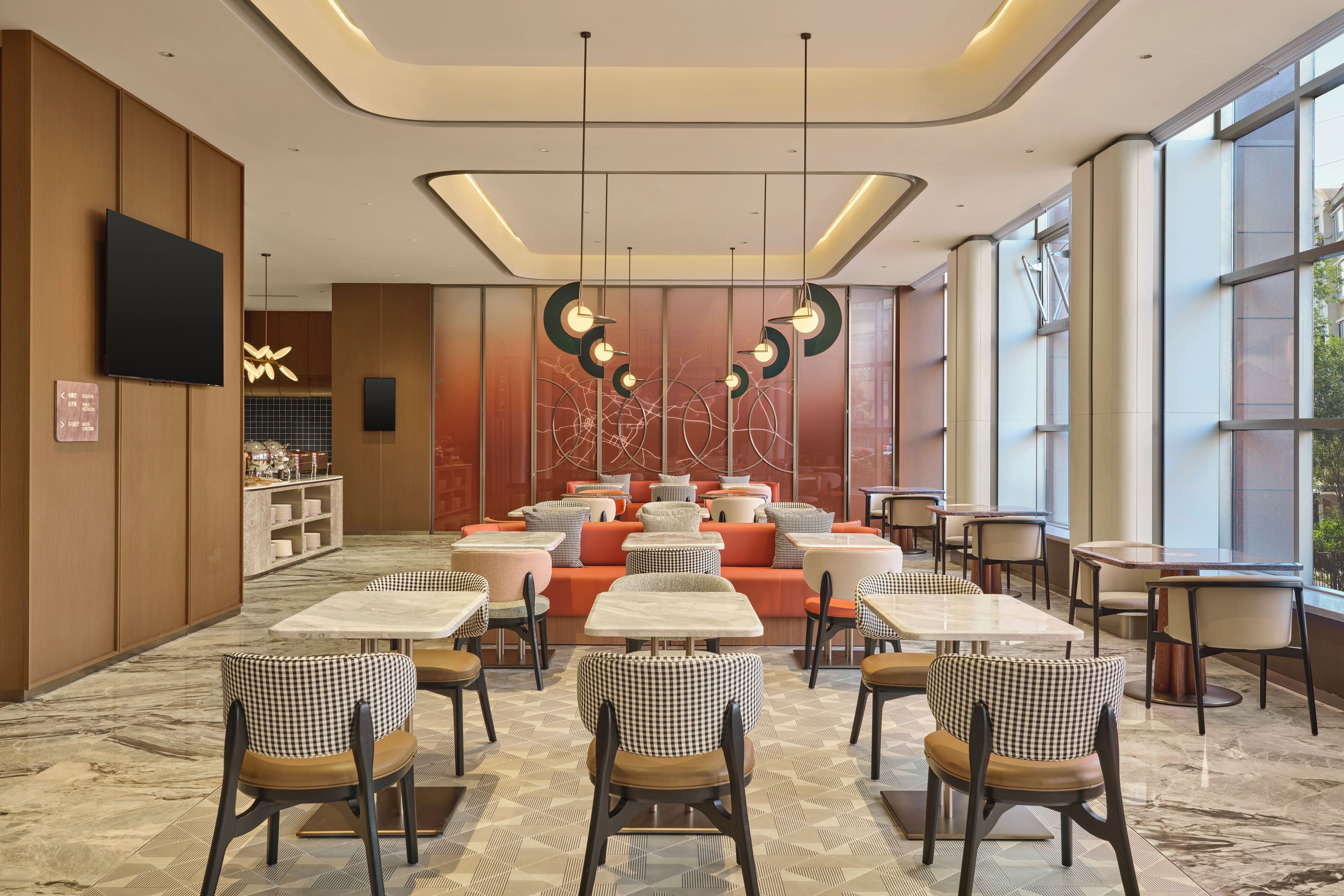 Een moderne eetruimte met geruite stoelen, ronde tafels en een centrale zithoek met oranje banken.